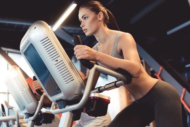 A woman exercises on a stationary bike in a modern gym, focusing on her fitness routine.