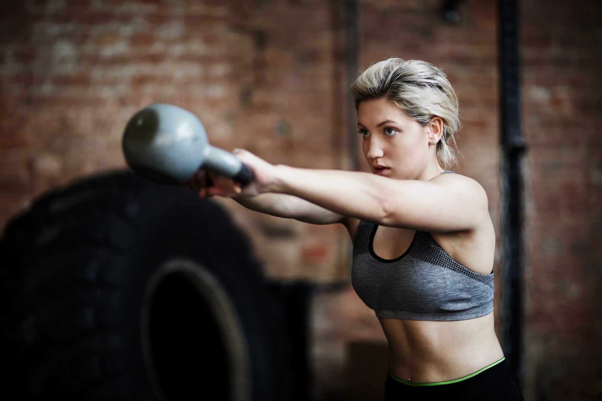 A woman in a sports bra holds a kettlebell, showcasing strength and fitness in an active workout setting.